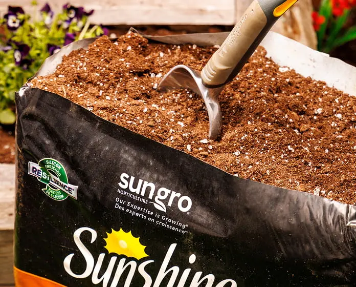 Sungro potting mix bag with shovel pouring soil into a raised garden bed.