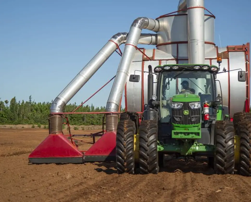 Green agricultural tractor in a large field with irrigation equipment.