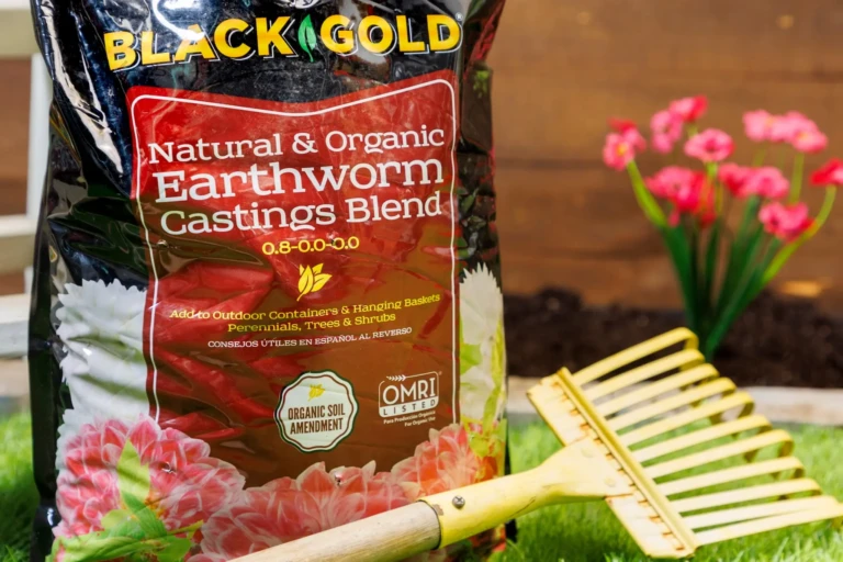 Close-up of Black Gold Natural & Organic Earthworm Castings Blend bag next to a wooden rake and pink flowers
