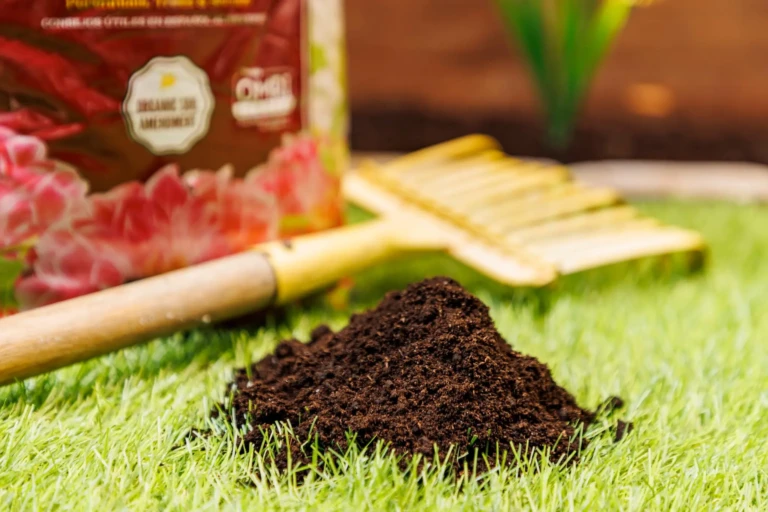Pile of dark organic potting mix on turf with a small yellow garden rake and SunGro branded bag in background