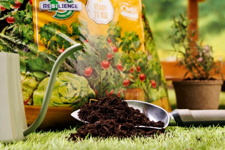 Close-up of a gardening scoop piled with dark potting mix on grass beside a watering can and SunGro potting soil bag