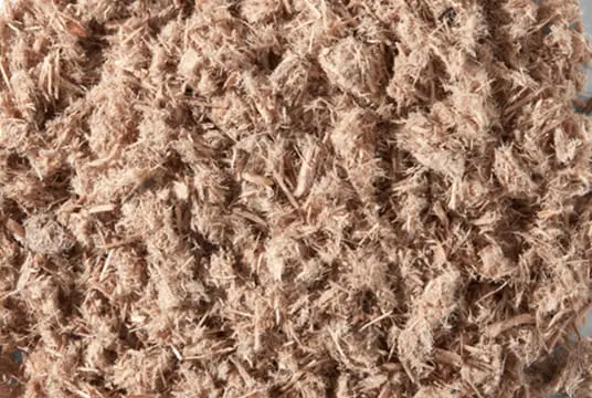 Close-up of shredded light brown wood fiber mulch with fibrous texture used for horticulture and soil improvement